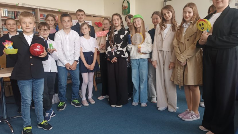 uczestnicy na niebieskim dywanie stojący uśmiechnięci w bibliotece z nagrodami