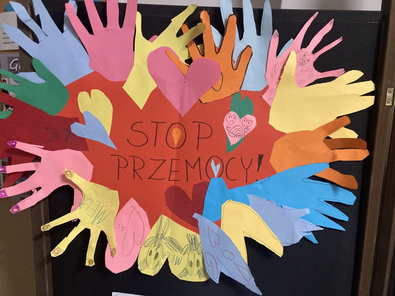 Wycięte z kolorowego papieru dłonie przyklejone wokół napisu STOP PRZEMOCY