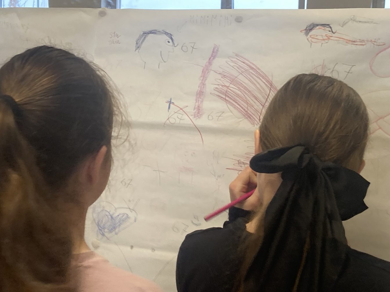 Dwie uczennice rysują na wielkiej kartce przyklejonej do luster (mural) w ramach akcji Dzieciństwo Bez Przemocy