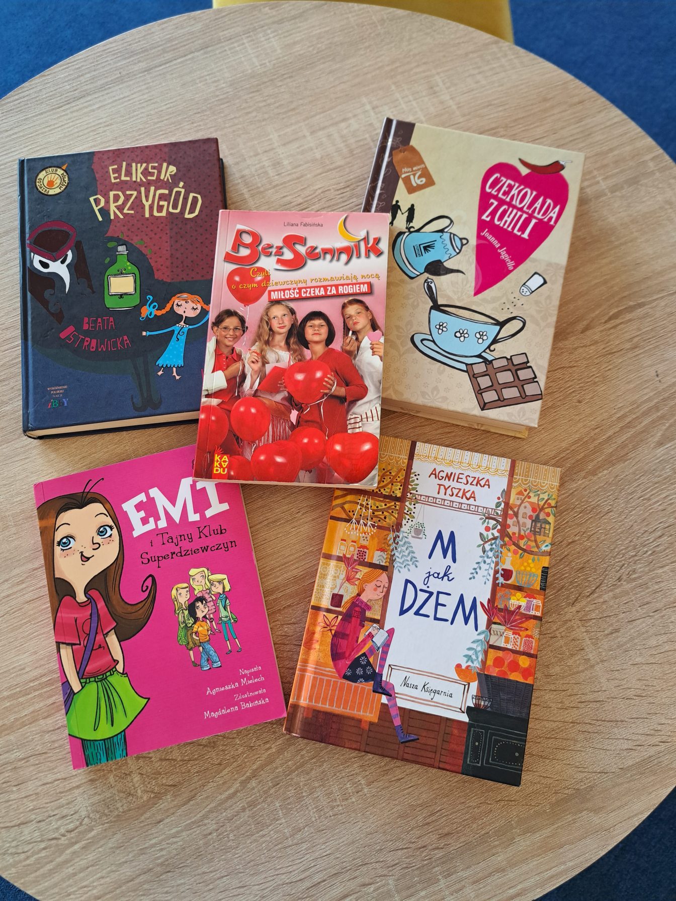  Zdjęcie z okładkami książek ; „Eliksir przygód”- brązowo –granatowa okładka z rysunkiem zielonego eliksiru oraz głową tajemniczej postaci i dziewczynki z warkoczami, „ BezSennik”- zdjęcie 4 nastolatek ubranych w białe lub czerwonesukienki trzymające czerwonebalony w kształce serc,  „ Czekolada z Chili”- jasno beżowe tło ,a na nim niebieski dzbanek z niebieską filiżanką ,
„ Emi i tajny klub superdziewczyn”- różowa okładka ,po lewo duża postać Emi a obok mniejsze postacie czterech dziewczynek, „ M jak dżem”- okładka w ciepłych kolorach różu i pomarańczu, dziewczynka czyta książkę , w tle regały z przetworami. 

