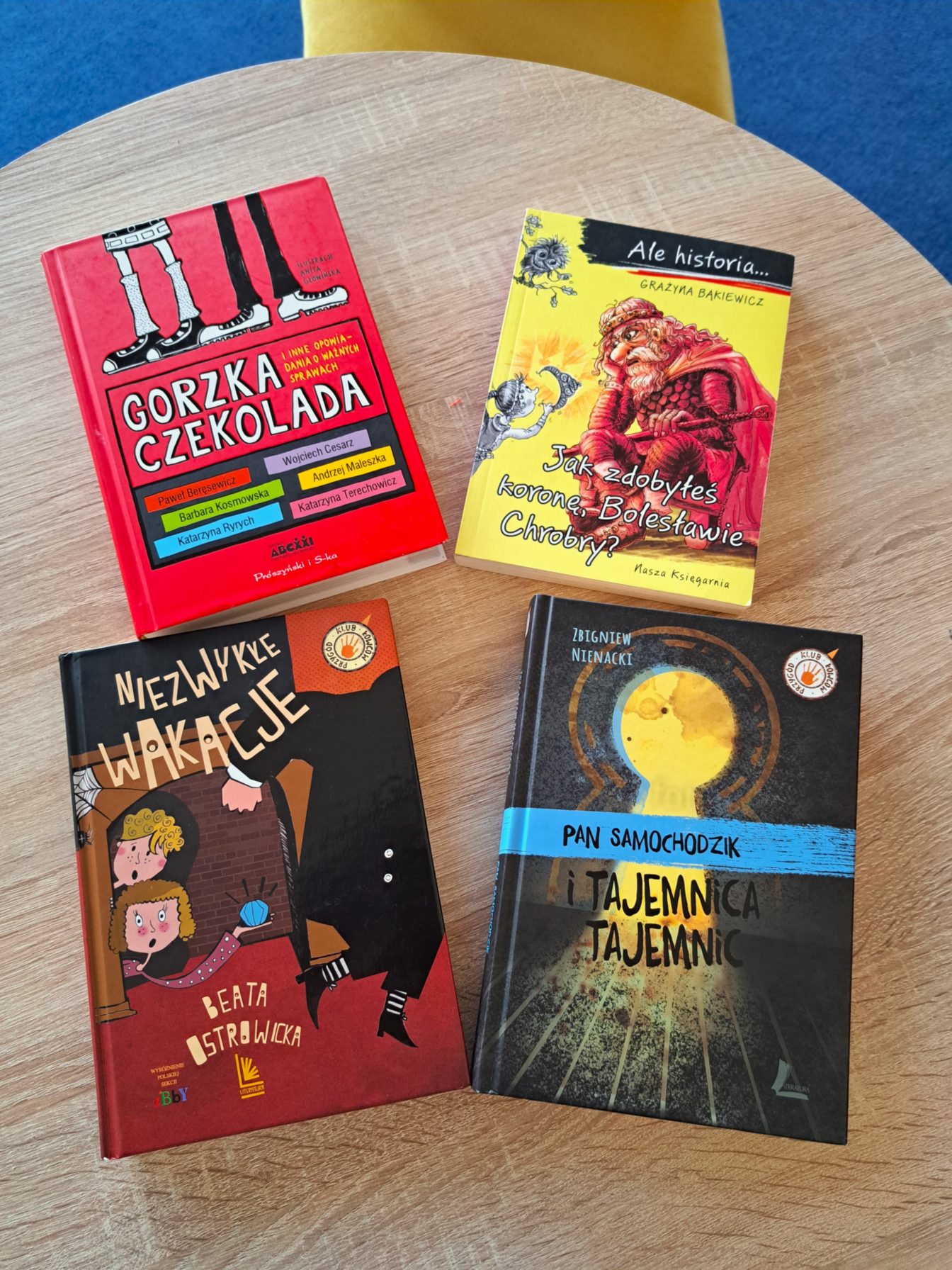 Zdjęcie z okładkami książek : „Gorzka czekolada”- okładka w kolorze czerwonym u góry widoczne nogi dzieci, „ Jak zdobyłeś koronę Bolesławie Chrobry” -żółta okładka w środku siedzi zamyślony król, „ Niezwykłe wakacje”- dwoje dzieci patrzących na umykającą postać,  „ Pan Samochodzik i tajemnica tajemnic”- czarna okładka z żółtą dziurką od klucza.
