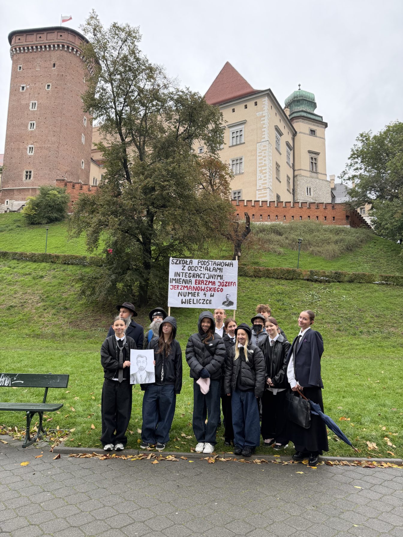 3. Zdjęcie grupowe uczniów na tle Wawelu z banerem szkoły i portretem E.J. Jerzmanowskiego..