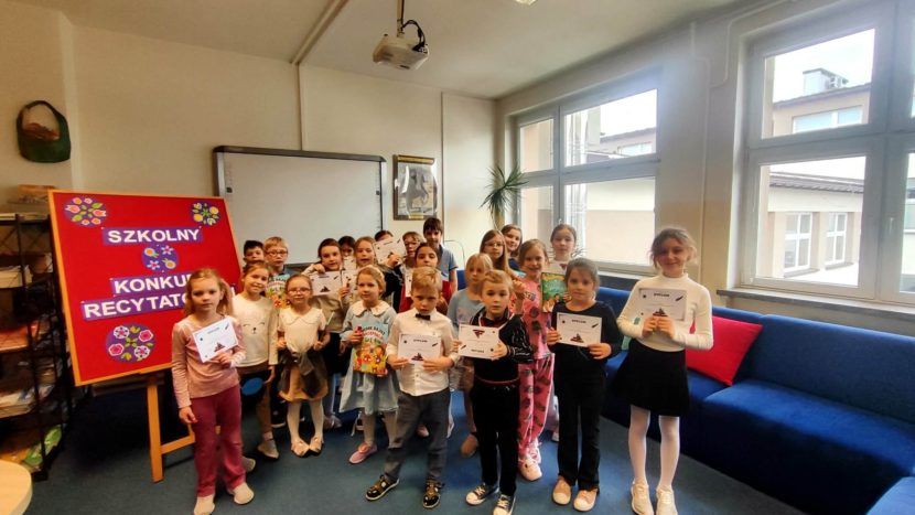 Uczestnicy konkursu recytatorskiego w bibliotece szkolnej z nagrodami pozują do zdjęcia