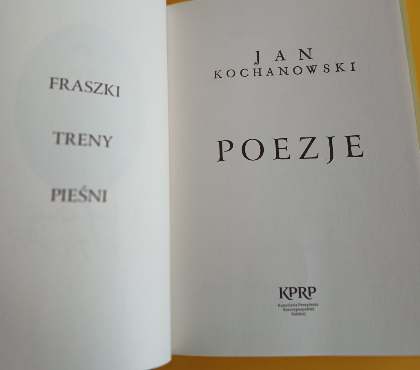 Zdjęcie przedstawia otwartą książkę. Z lewej strony napis: Fraszki, Treny, Pieśni.
Po prawej stronie Jan Kochanowski - Poezje.