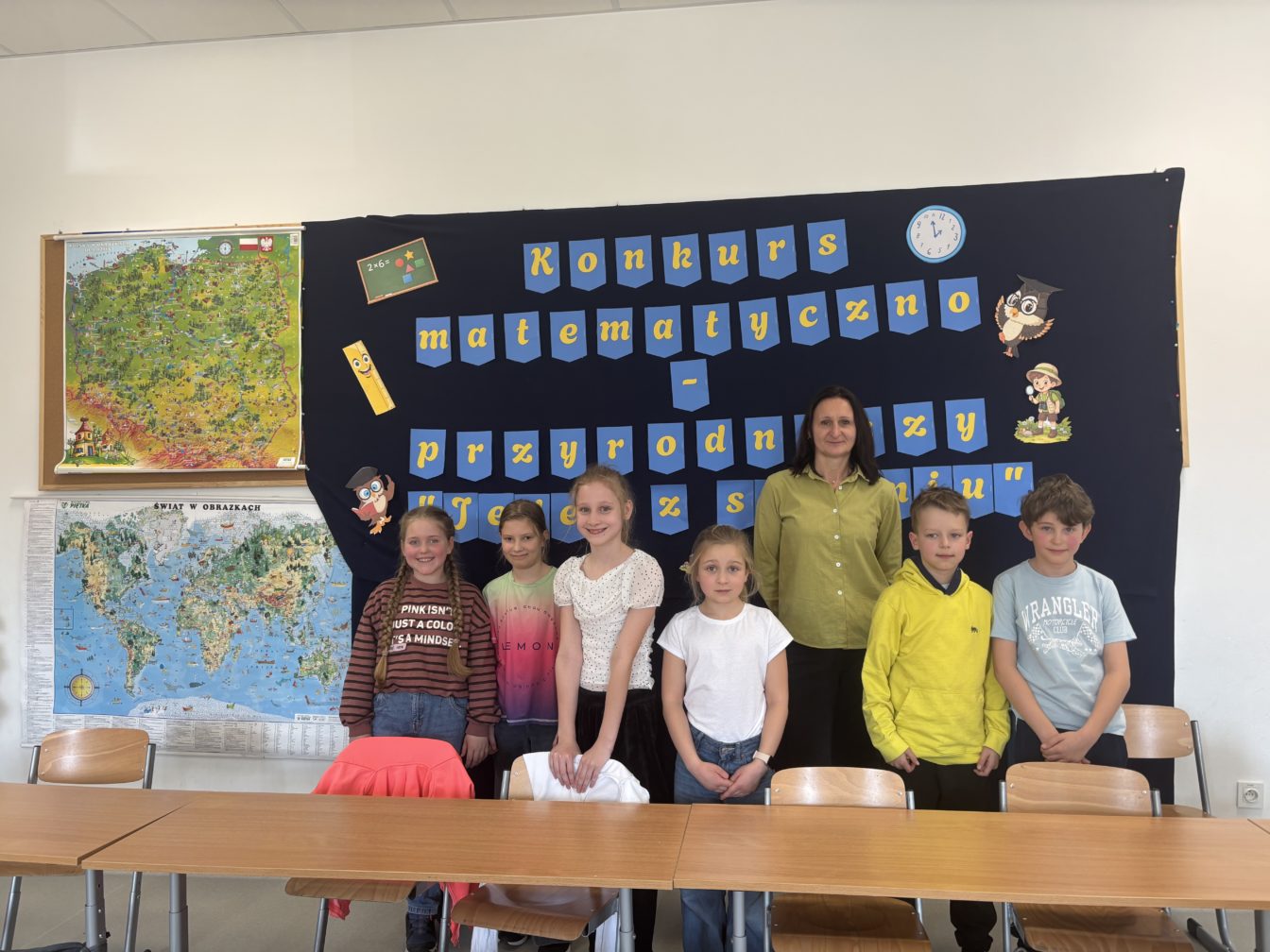 Uczniowie klas III SPnr4 wraz z Panią wicedyrektor na tle dekoracji przygotowanej na Szkolny Konkurs Matematyczno-Przyrodniczy „Jeden z siedmiu”.