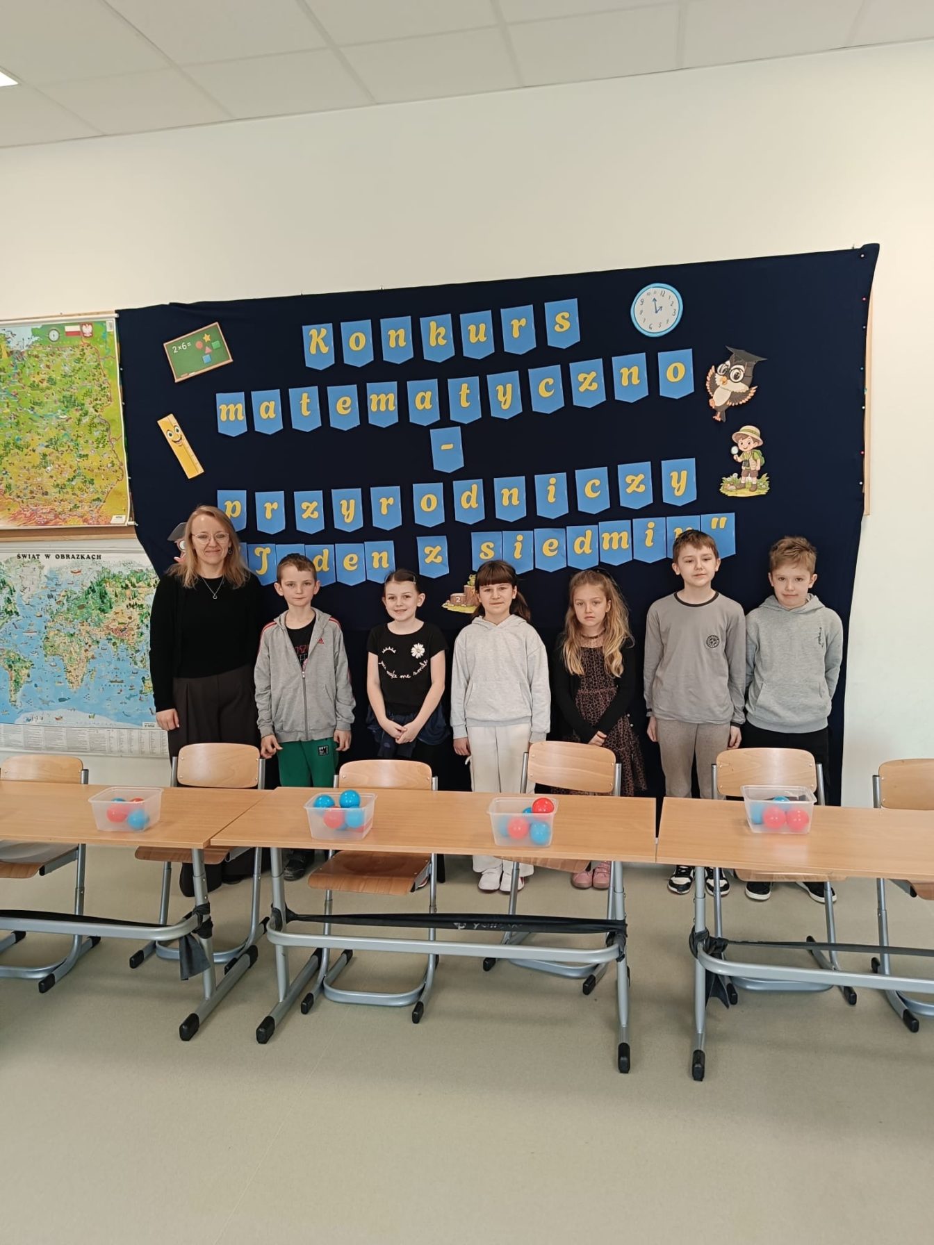 Uczniowie klas III SPnr4 wraz z Panią wicedyrektor na tle dekoracji przygotowanej na Szkolny Konkurs Matematyczno-Przyrodniczy „Jeden z siedmiu”.