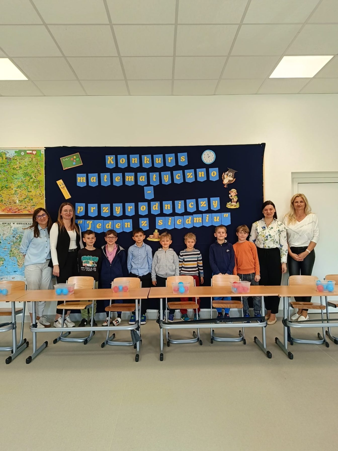 Uczniowie klas II SPnr4 wraz z Panią wicedyrektor na tle dekoracji przygotowanej na Szkolny Konkurs Matematyczno-Przyrodniczy „Jeden z siedmiu”.